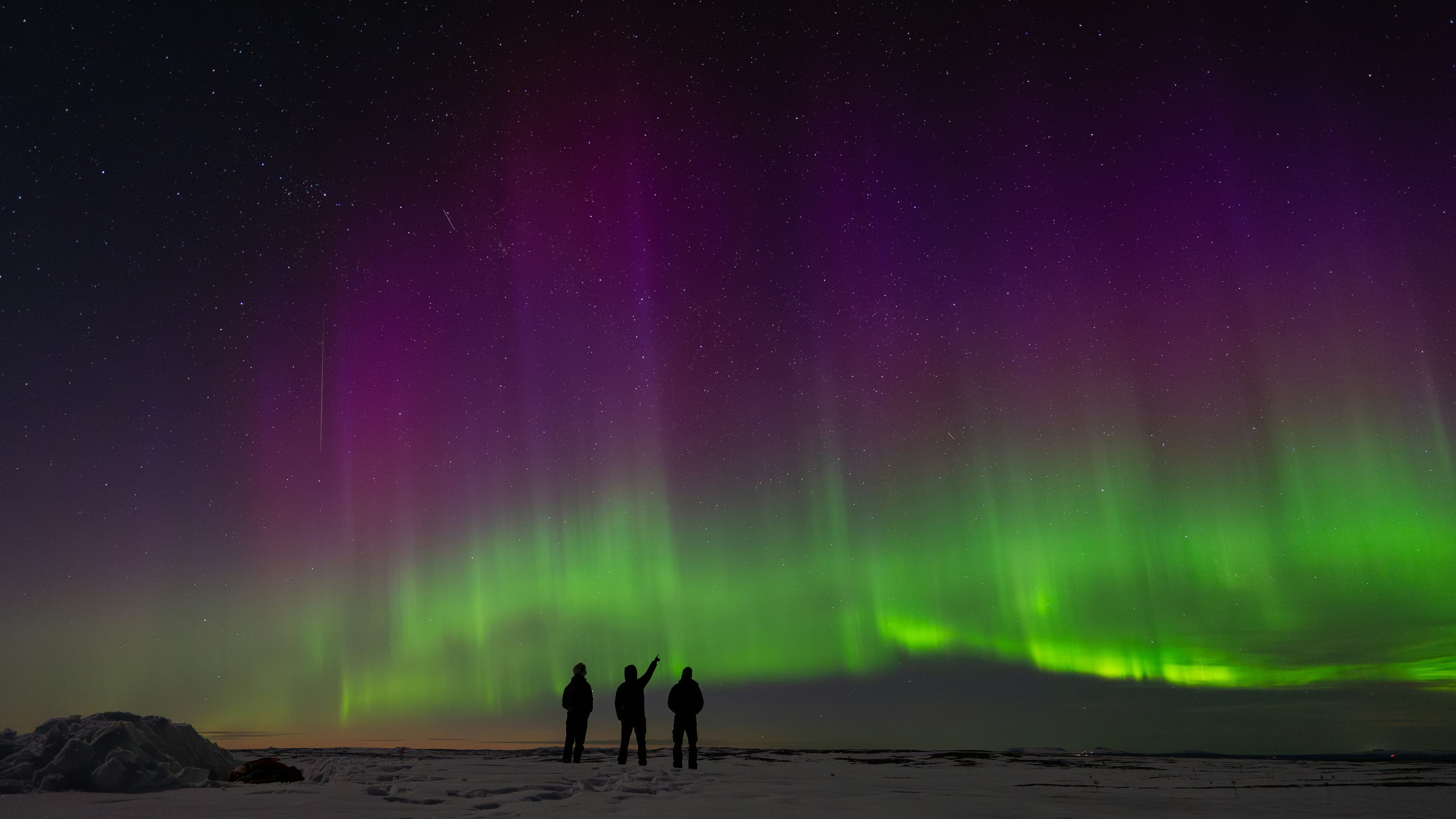 Three people under the northern lights